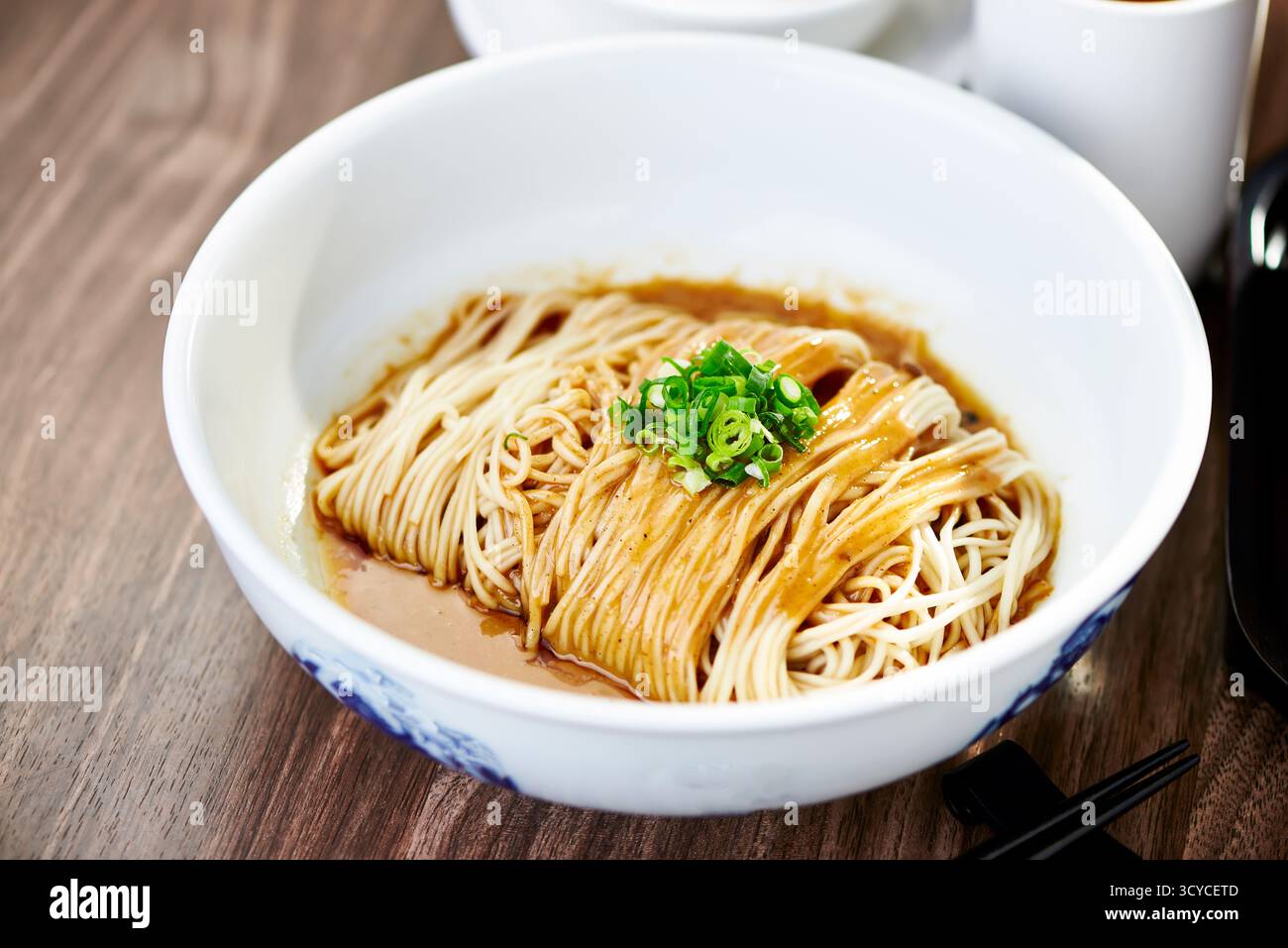 Köstliche Nudeln mit Sesamsauce, garniert mit frischen grünen Zwiebeln, serviert in der Schüssel, Seitenansicht des chinesischen Gerichts Stockfoto