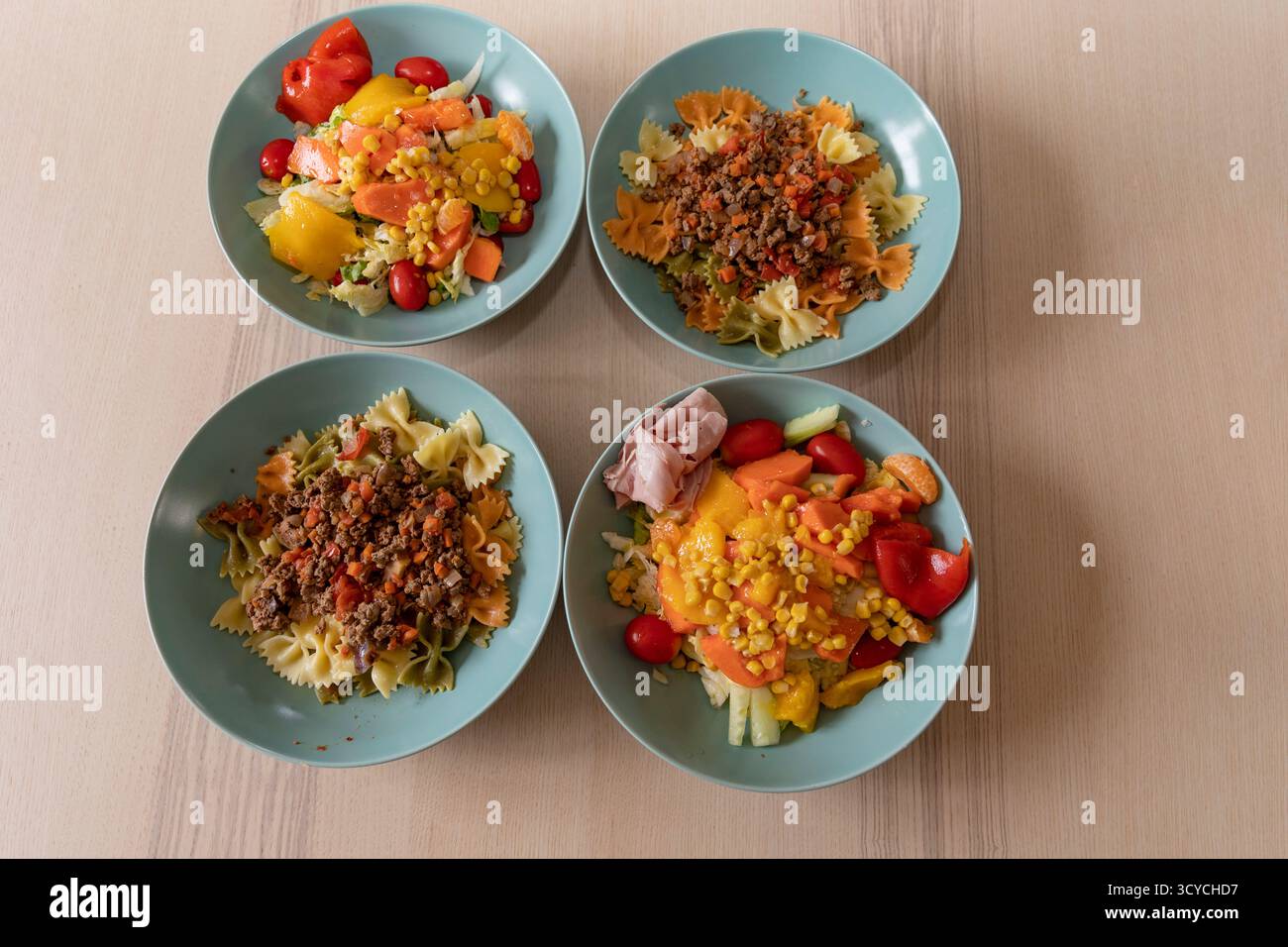 Hausgemachtes Mittagessen mit Pasta, frischem Gemüsesalat und Drachenfrüchten, die in türkisfarbenen Schüsseln auf Holztisch angeordnet sind. Stockfoto