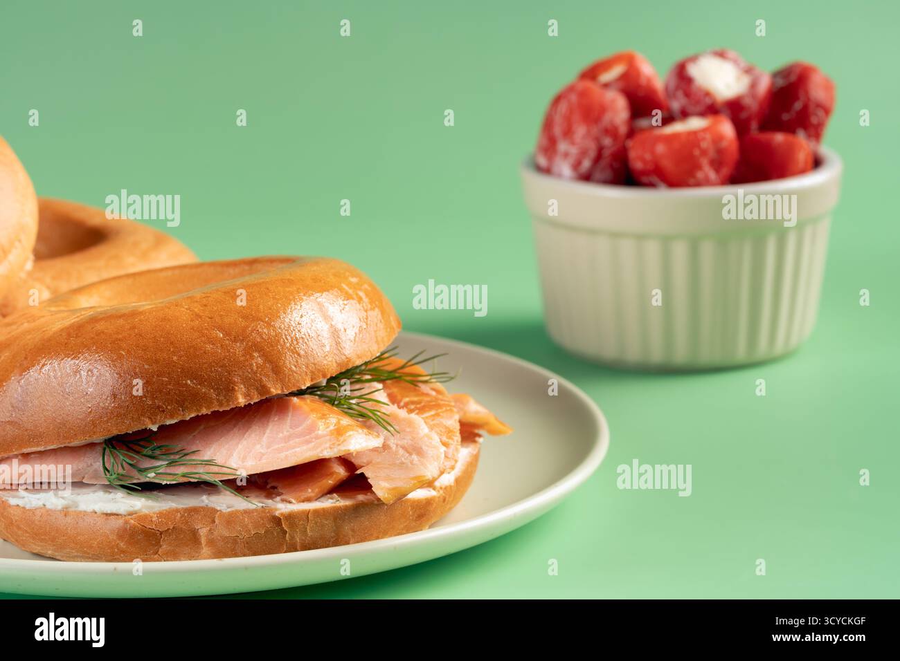 Ein Bagel mit Lachs und Dill ist auf einem weißen Teller. Neben dem Sandwich gibt es eine Schüssel mit Kirschtomaten Stockfoto