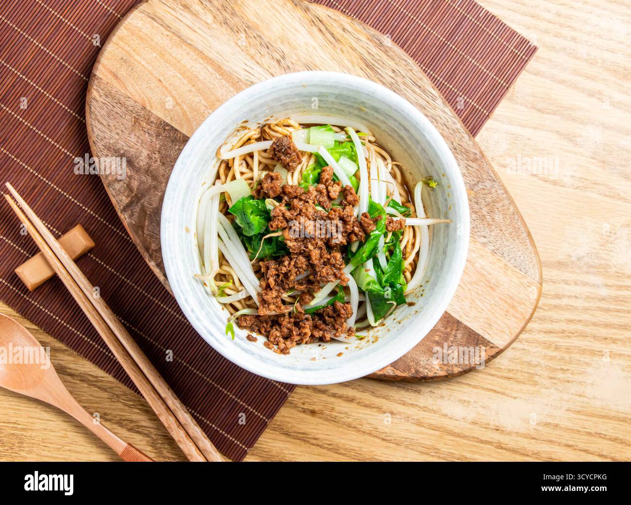 Dan Dan Noodles mit gemahlenem Schweinefleisch in Sesamsauce serviert in einer Schüssel mit Essstäbchen und Löffel isoliert auf Holzbrett Seitenansicht von taiwanischen Speisen Stockfoto