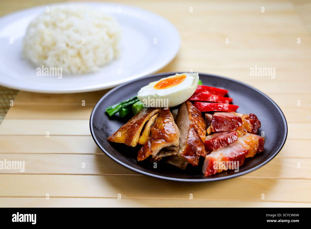 Gebratene Ente und Char Siu mit Reis und gesalzenem gekochtem Ei serviert auf einem Teller isoliert auf dem Tisch, Seitenansicht von Hong Kong Essen Stockfoto