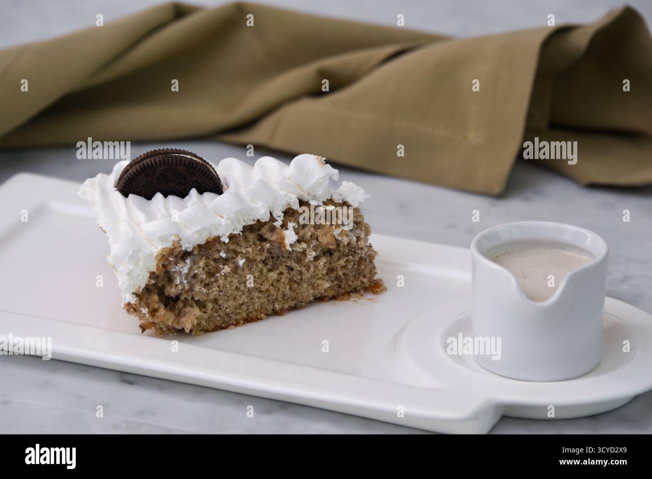Oreo Cream Cake Slice mit zerkleinerten Schokoladen-Sandwichkeksen, gebacken mit Schlagsahne mit Milchsauce, serviert auf einem Teller mit isolierter Serviette Stockfoto