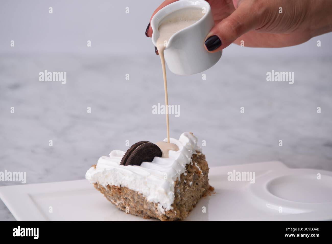 Oreo Cream Cake Slice mit zerkleinerten Schokoladen-Sandwichkeksen, garniert mit Schlagsahne und tropfender Milchsauce, serviert auf einem Teller, der auf Background isoliert wird Stockfoto