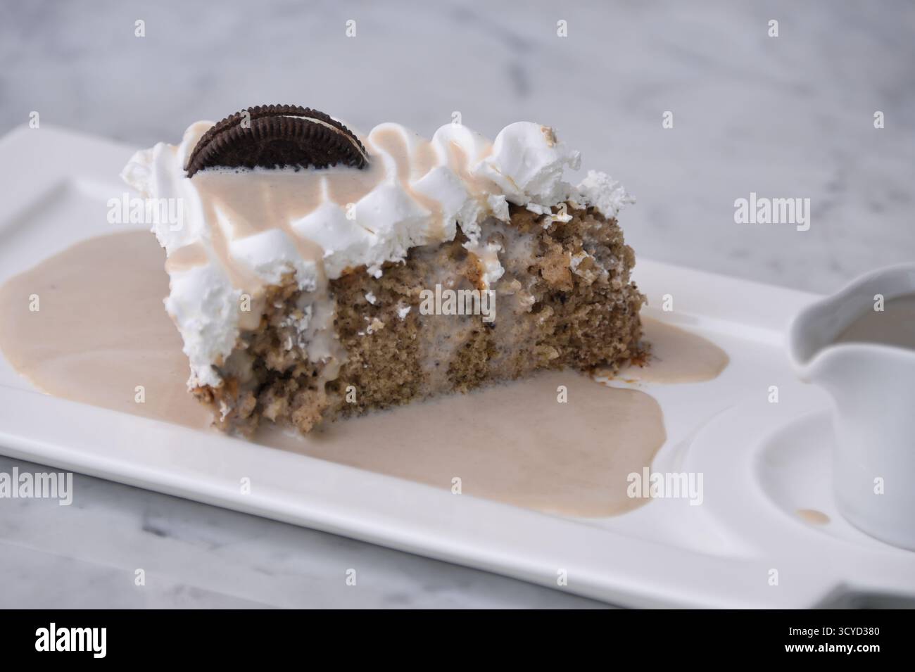 Oreo Cream Cake Slice mit zerkleinerten Schokoladen-Sandwichkeksen, garniert mit Schlagsahne mit tropfender Milchsauce serviert auf einem Teller, der auf dem Hintergrund isoliert ist Stockfoto