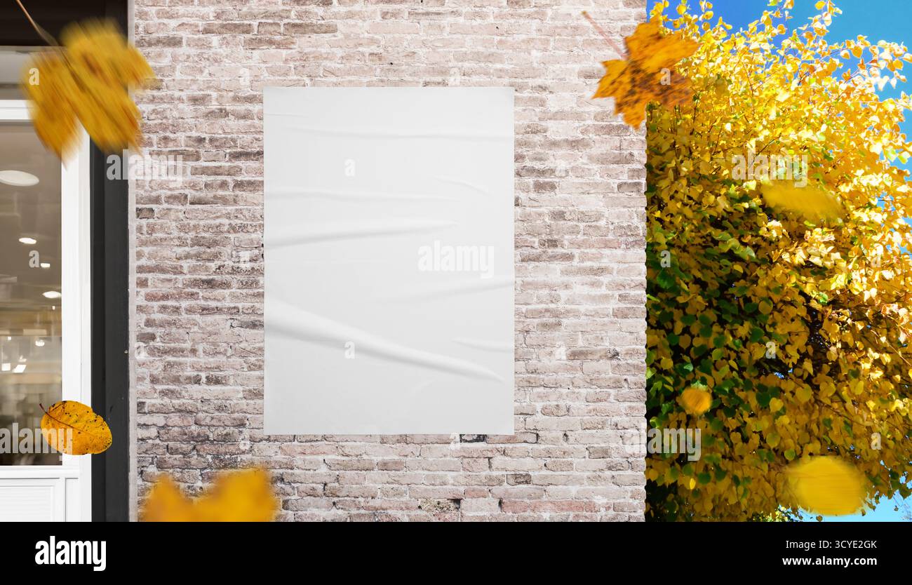 Weißes Poster an Ziegelwänden mit gelben Blättern in Bewegung, ideal für Mockups für Außenwerbung und saisonale Kampagnenbilder Stockfoto