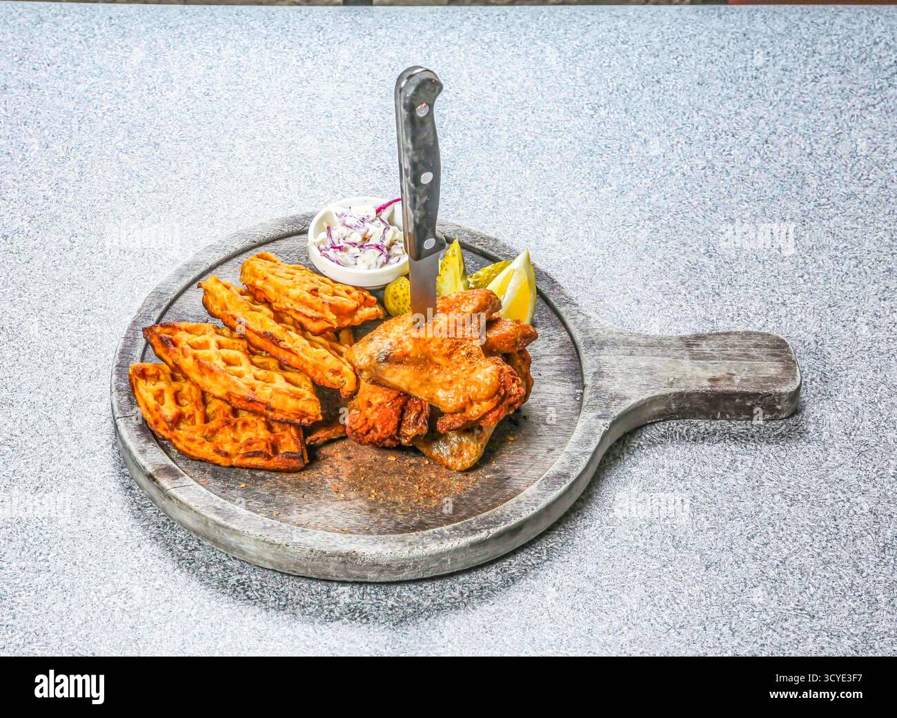 Chicken Wings and Waffles beinhaltet ein Messer, das in das Essen eine Seite von Krautsalat gesteckt wurde, und Zitronenscheiben, die auf einem Holzbrett serviert werden, Seitenansicht von hongkong-Speisen Stockfoto
