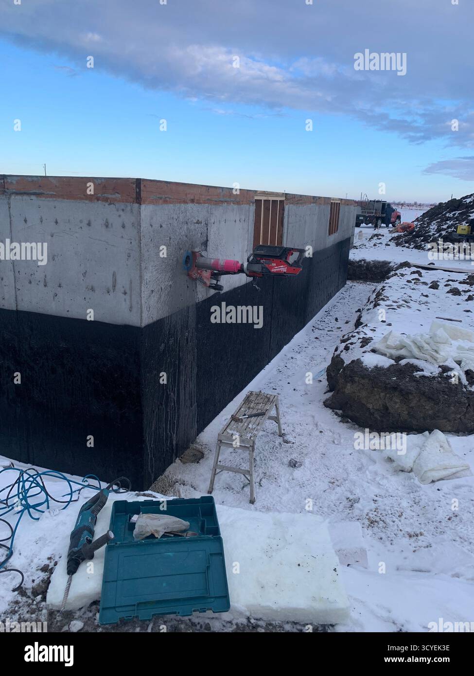 Milwaukee Kernbohrer, der auf einem Betonfundament in einer verschneiten Umgebung im Freien arbeitet. - Smartphone-aufgenommenes Stockfoto