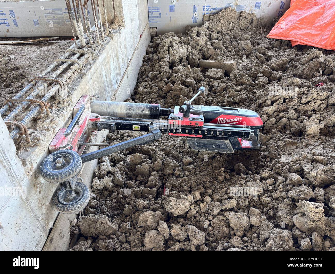 Milwaukee Betonkernbohrer in Aktion auf einer Baustelle mit Bewehrung und Schmutz. - Smartphone-aufgenommenes Stockfoto