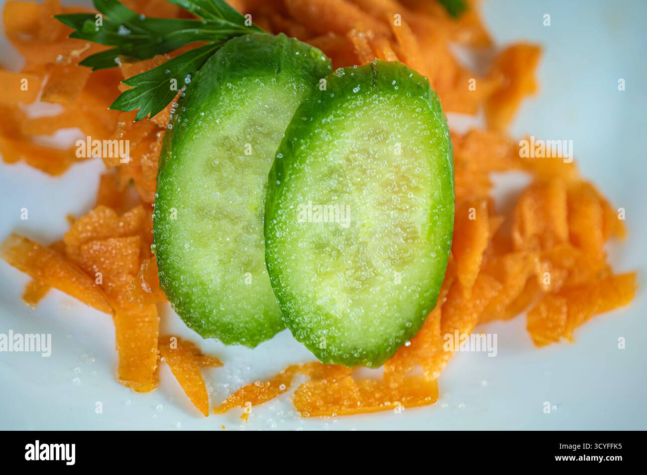 Geriebene saftige Karotten mit Petersilienblättern und Gurkenscheiben auf weißer Platte — Top View gesunde Lebensmittel Fotografie Stockfoto
