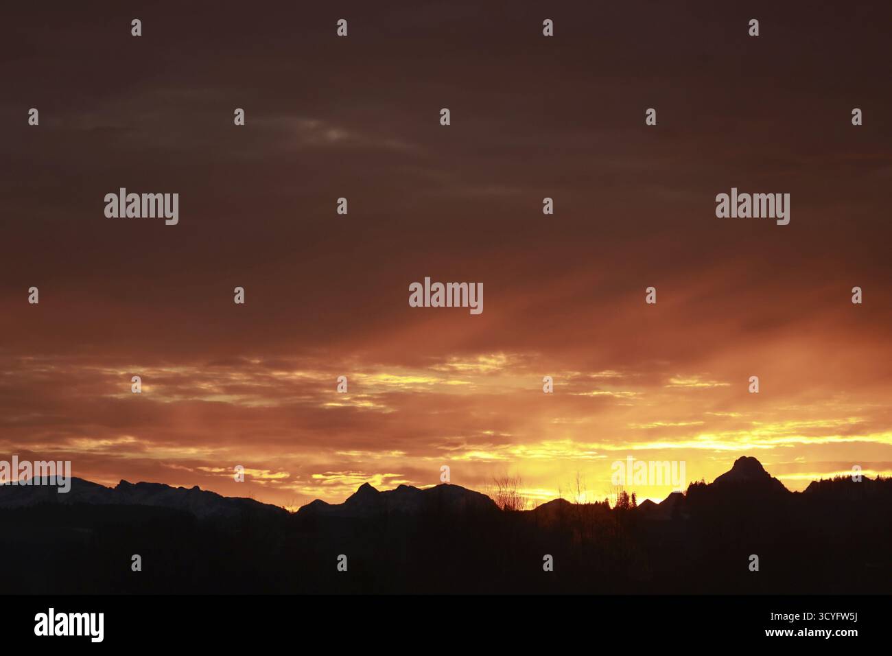 Der Himmel ist orange und die Berge sind im Hintergrund. Die Sonne untergeht und der Himmel ist voller Wolken Stockfoto