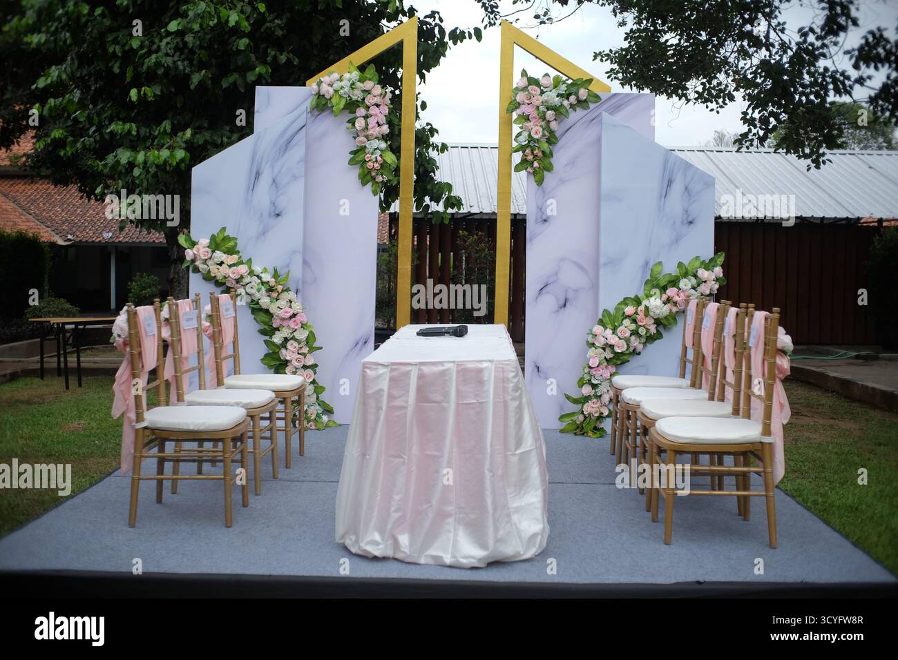 Stellen Sie Stühle und Tischdekorationen für eine Zeremonie auf, um ein Hochzeitsgelübde in einem Garten zu sagen. Stockfoto