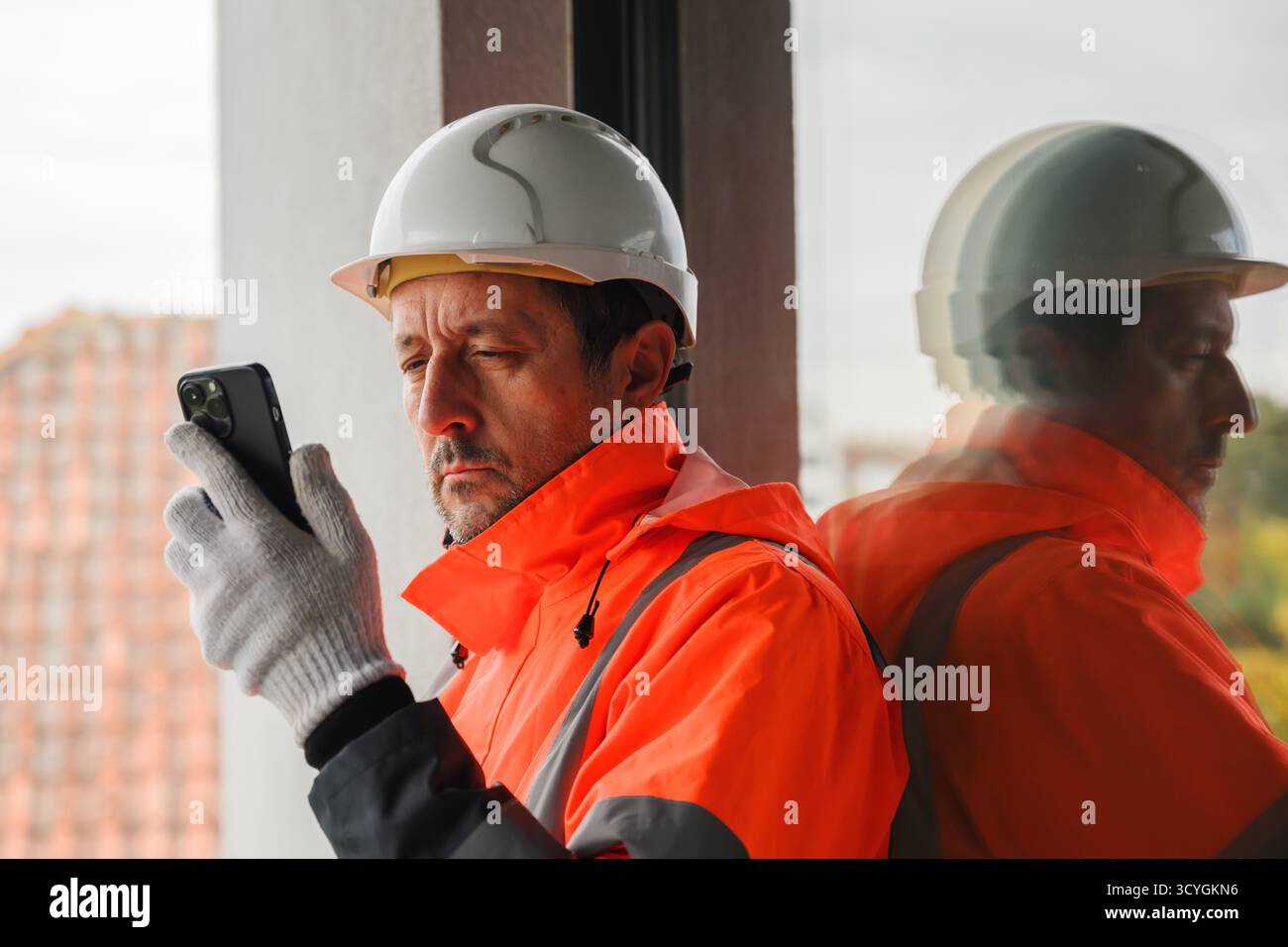 Bauingenieur mit Sicherheitsjacke und Schutzhelm mit Smartphone auf der Baustelle, Konzept der Kommunikation, Planung und moderne Technik in e Stockfoto