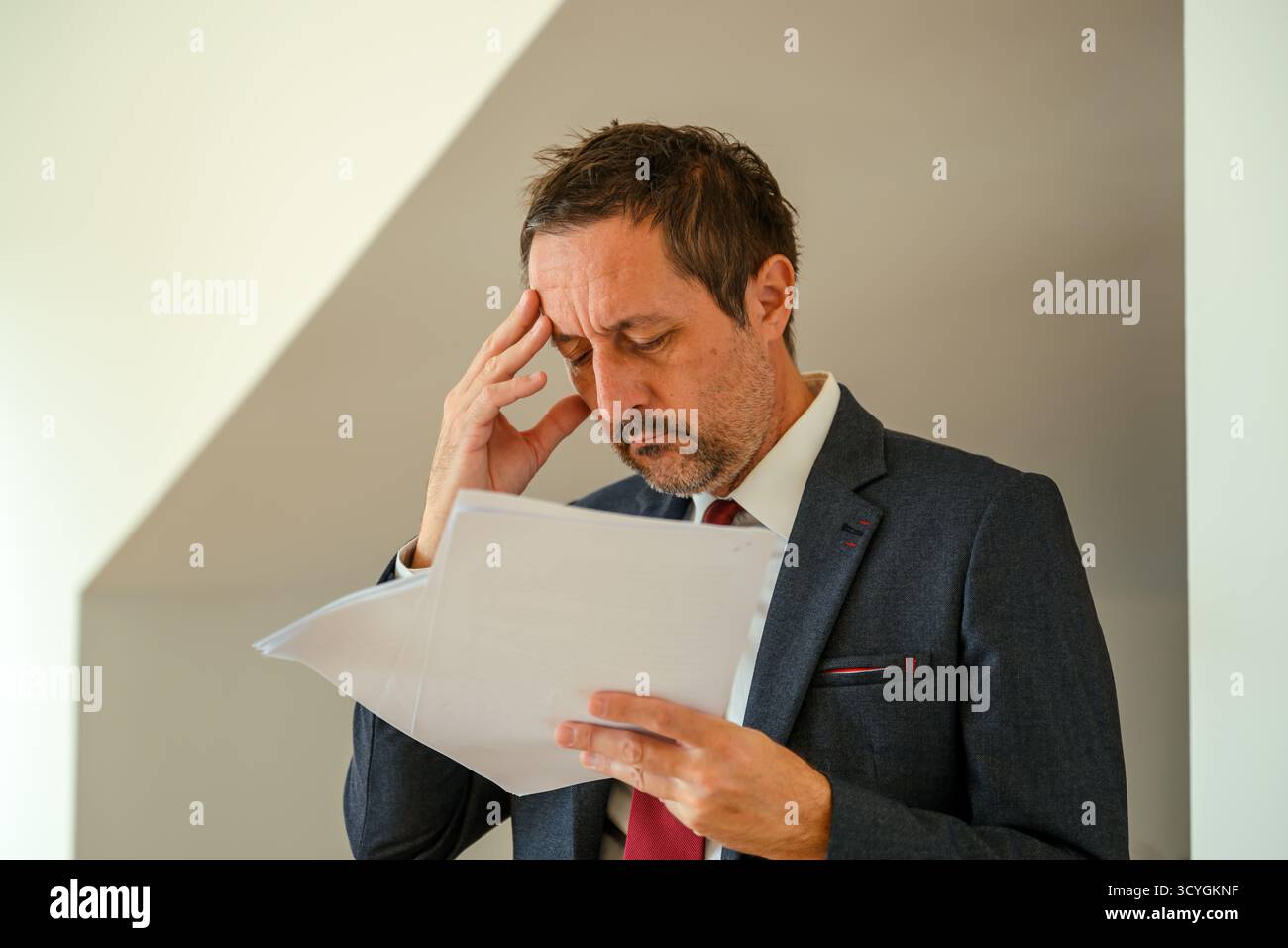 Besorgter Geschäftsmann im Anzug, der Finanzdokumente liest, durch negative Berichte gestresst, Papierkram überprüft und unter Stress am Arbeitsplatz leidet. Selektiv Stockfoto