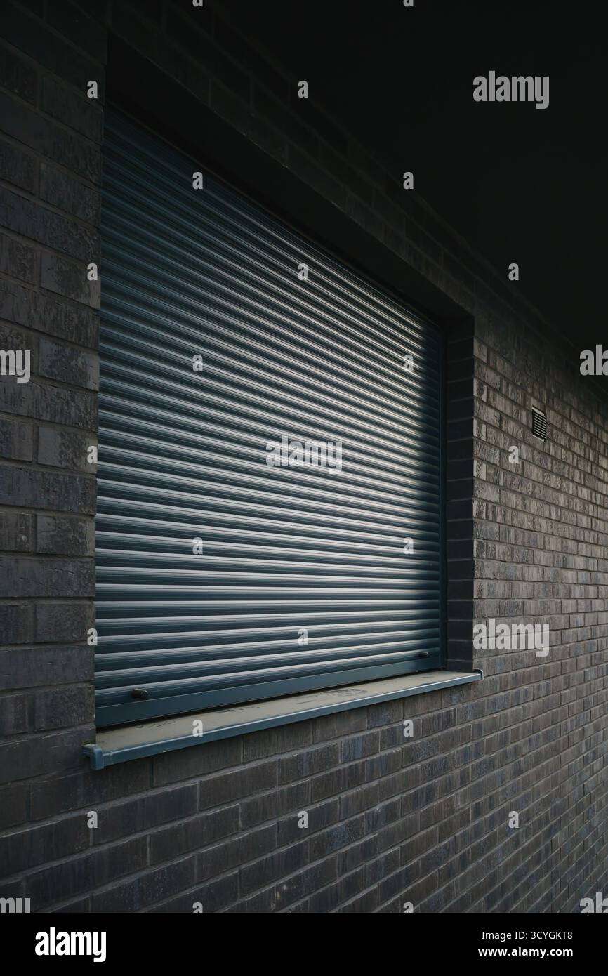 Geschlossener Rollladen aus Metall an einer modernen Ziegelwand, Sicherheits- und Datenschutzkonzept. Selektiver Fokus. Stockfoto