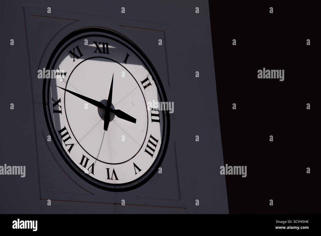 Eine Uhr mit römischen Ziffern steht auf 12 Uhr. Die Uhr steht in einem dunklen Raum Stockfoto