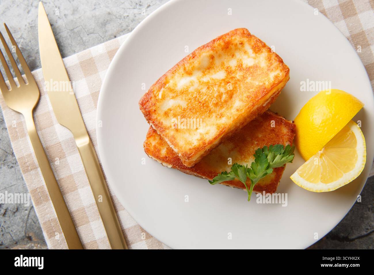 Saganaki ist eine griechische Delikatesse aus frittiertem Käse mit einem Zitronenkeil in Nahaufnahme auf einem Teller auf dem Tisch. Horizontale Draufsicht von oben Stockfoto