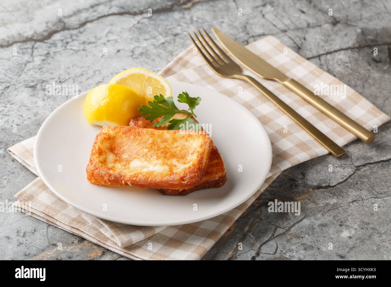Saganaki ist eine sehr beliebte griechische Vorspeise mit in der Pfanne angebratenem Käse, der neben Zitronenscheiben in Nahaufnahme auf einem Teller auf dem Tisch serviert wird. Horizontal Stockfoto