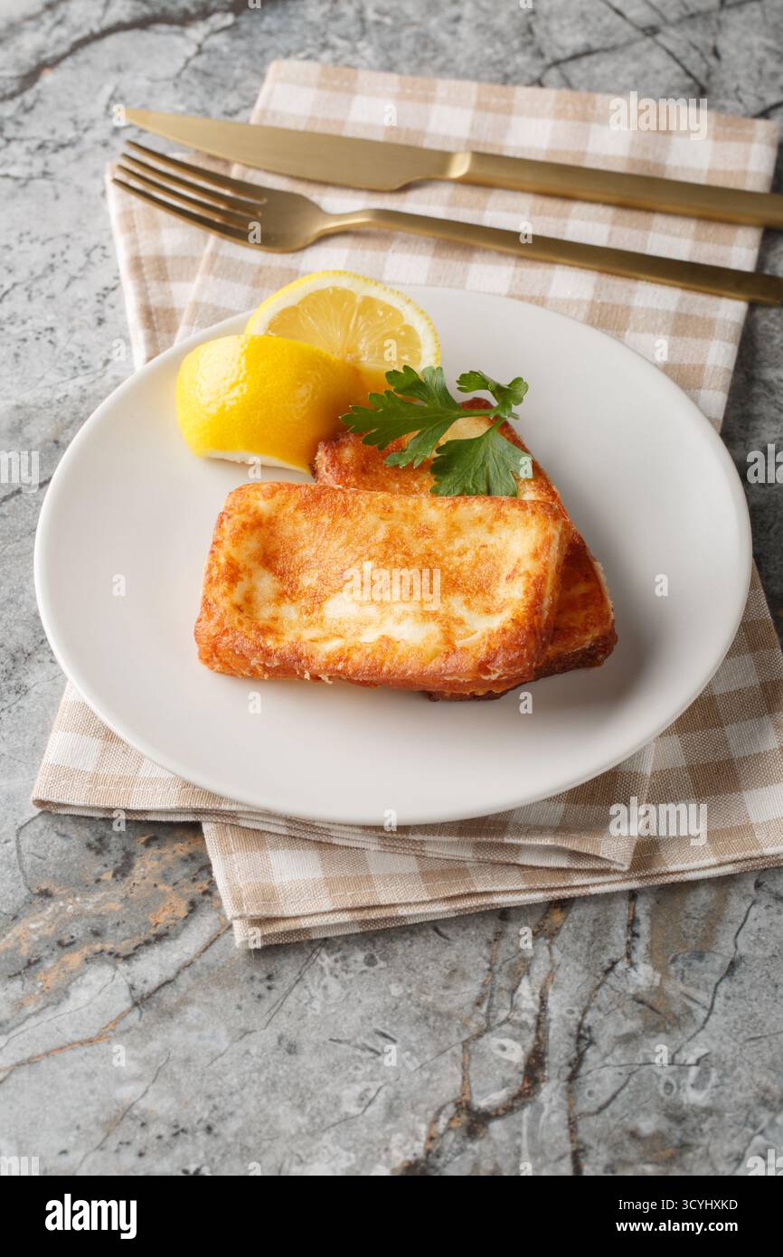 Leichte griechische Vorspeise Saganaki mit gebratenem Käse, serviert mit einem Zitronenkeil in Nahaufnahme auf einem Teller auf dem Tisch. Vertikal Stockfoto