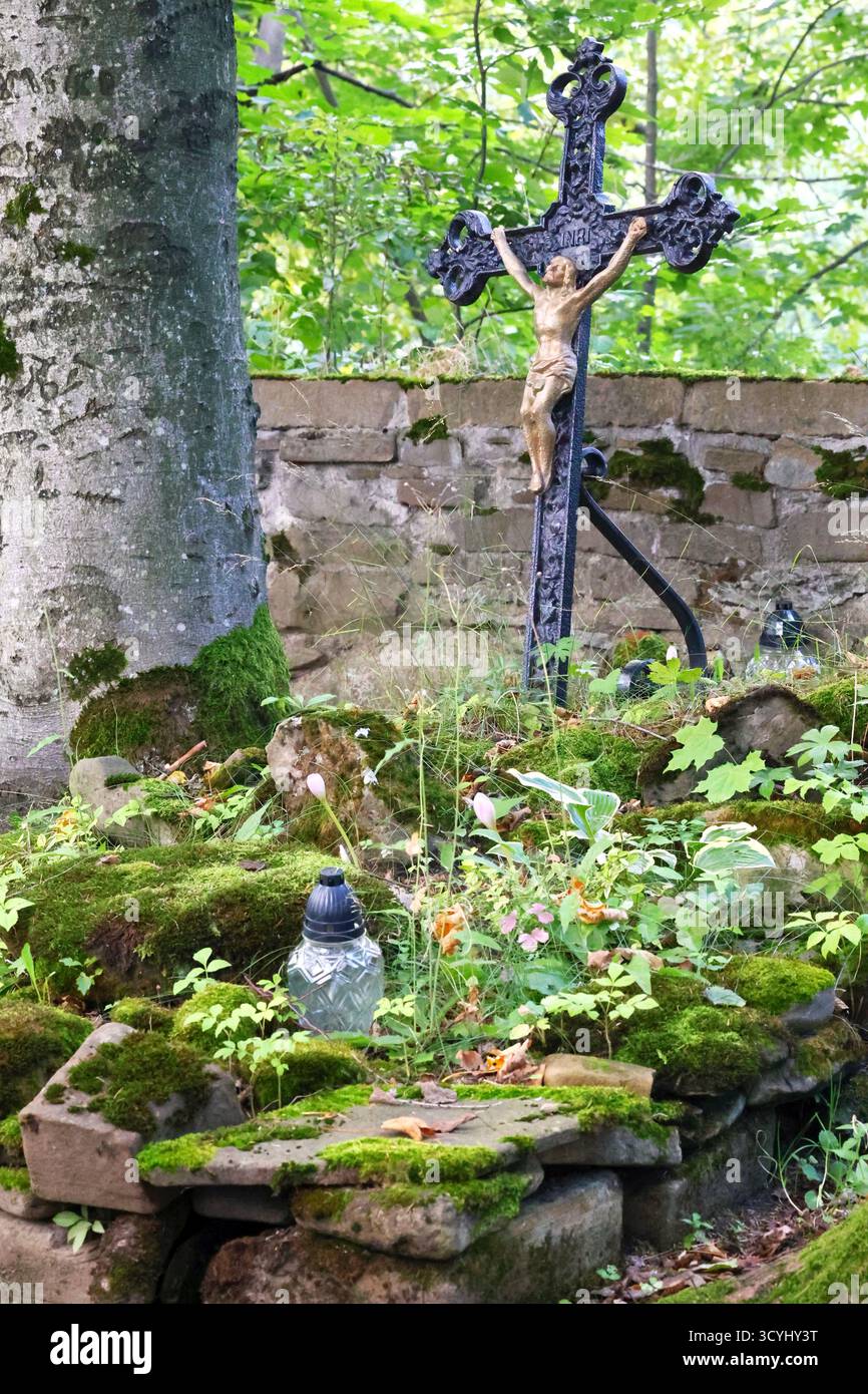 Bewachsenes Grab mit Laternen, Blumen, Kruzifix und Steinschnitzereien auf dem Friedhof Stockfoto