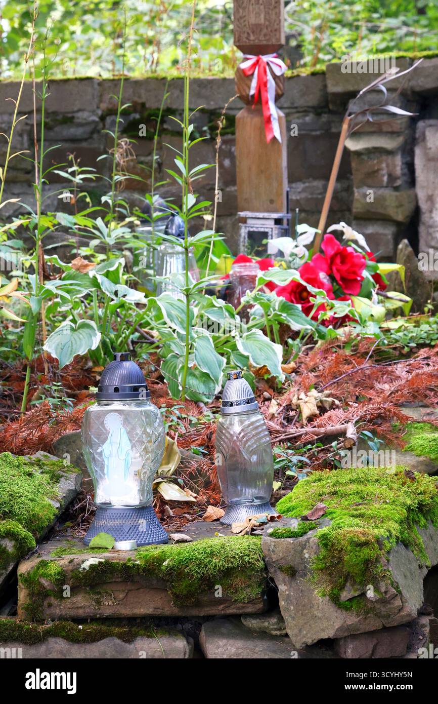 Bewachsenes Grab mit Laternen, Blumen, Kruzifix und Steinschnitzereien auf dem Friedhof Stockfoto