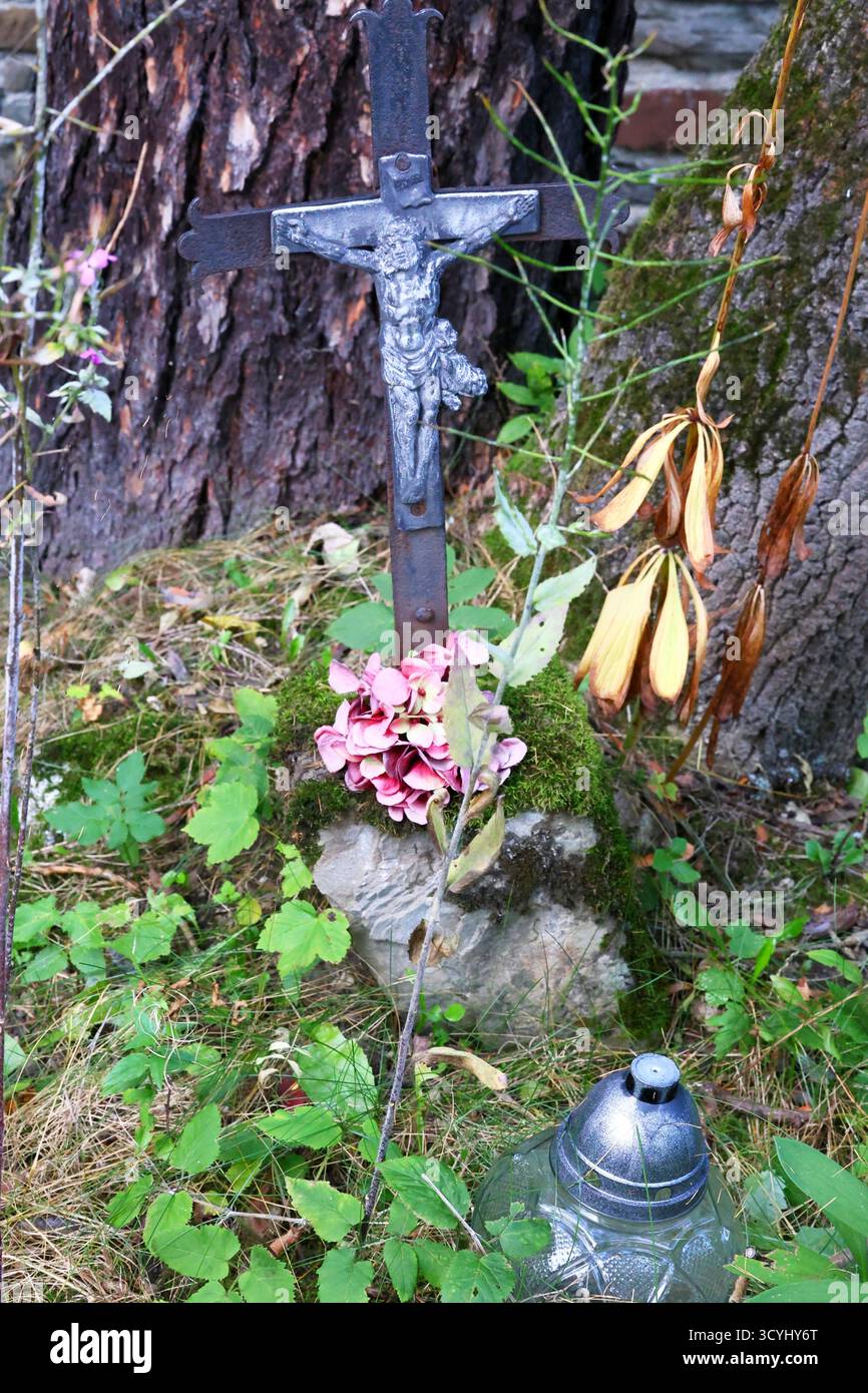 Bewachsenes Grab mit Laternen, Blumen, Kruzifix und Steinschnitzereien auf dem Friedhof Stockfoto