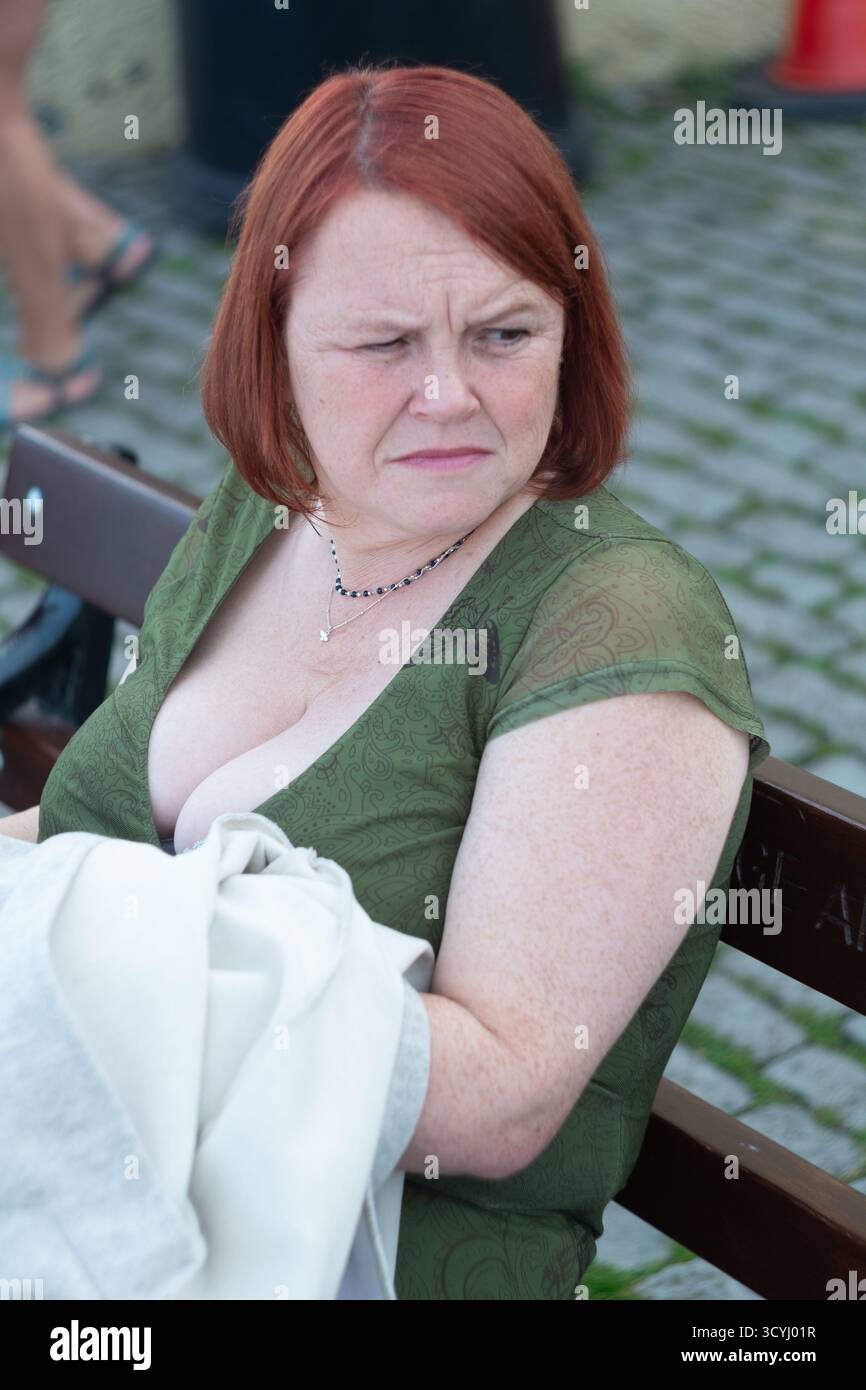 Frau mittleren Alters mit roten Haaren in grüner Oberseite, die auf der Bank mit kontemplativem Ausdruck sitzt Stockfoto