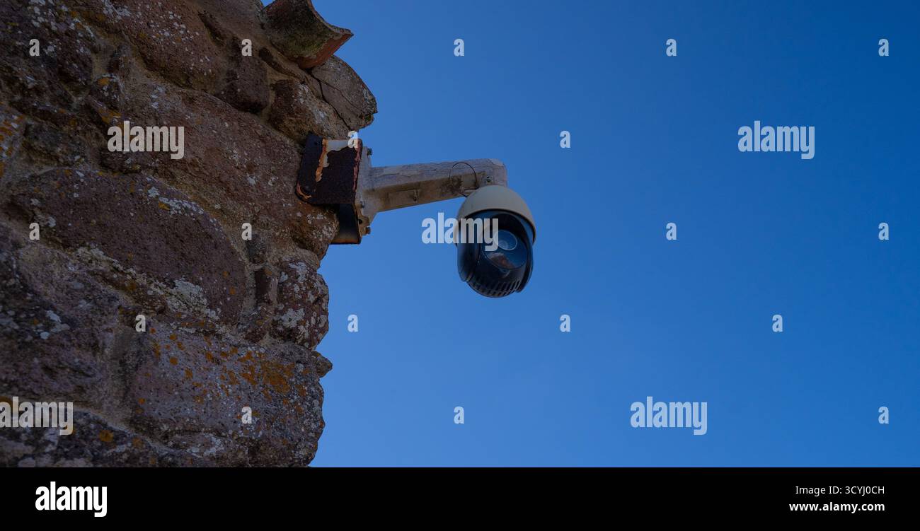 Überwachungskamera an einer alten Steinmauer unter hellblauem Himmel, Konzept der Sicherheit und Kontrolle. Stockfoto