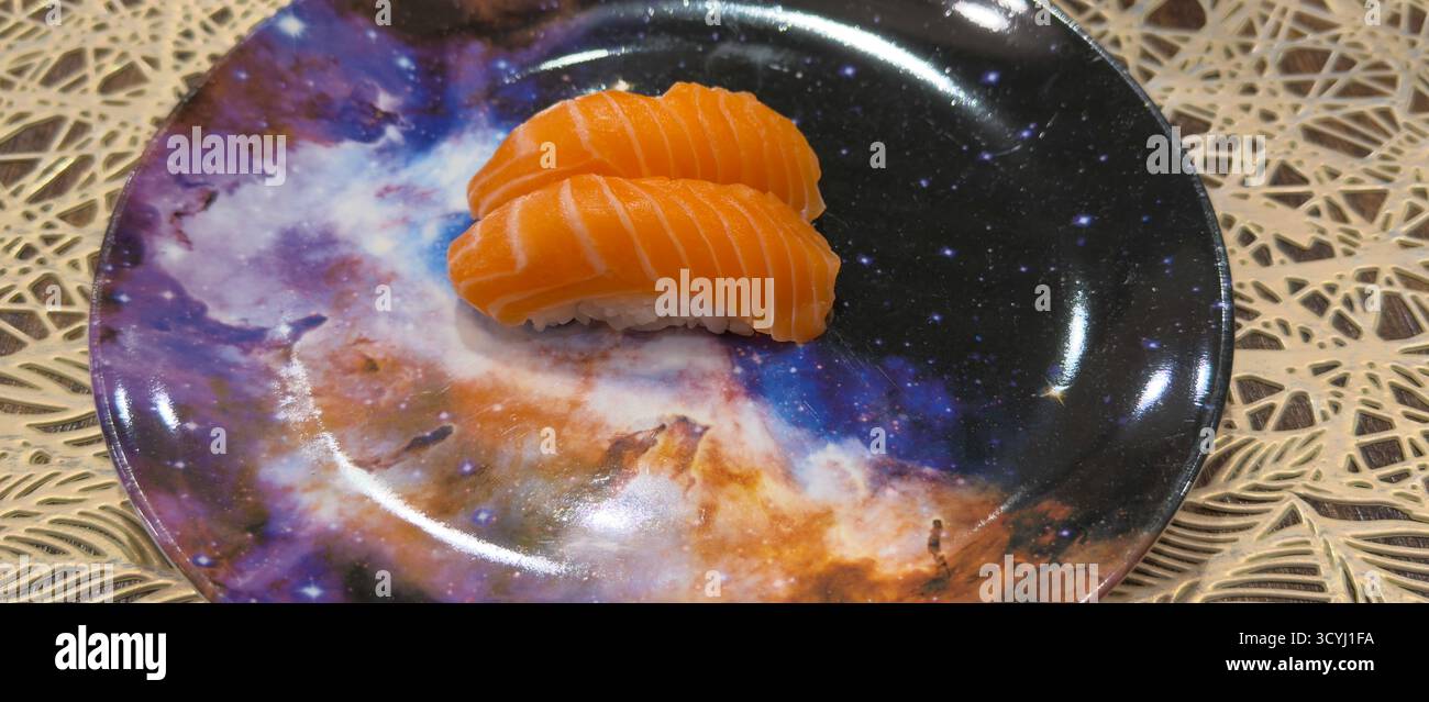 Zwei Stücke frischer Lachs-Nigiri-Sushi, wunderschön präsentiert auf einem Teller mit Galaxienmuster. Stockfoto