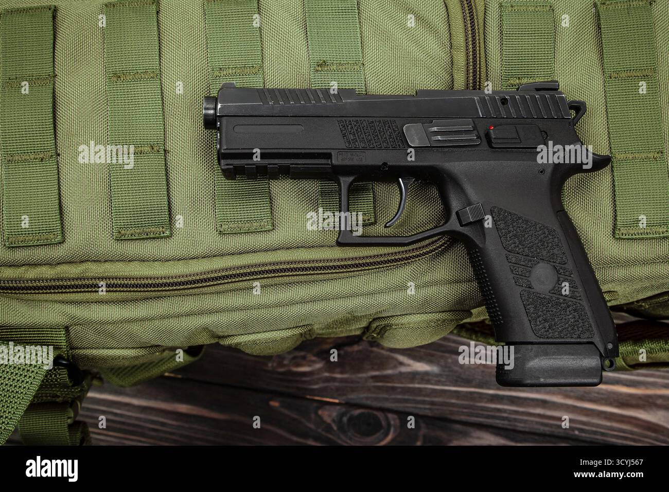Schwarze halbautomatische Pistole auf olivgrünem taktischem Gurtband und dunkler Holzoberfläche Stockfoto