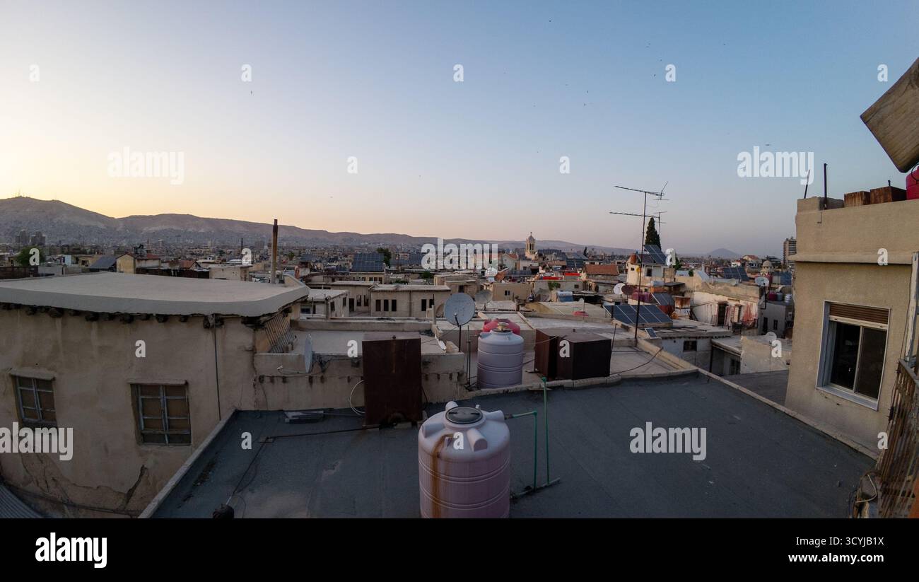 Panoramablick auf die Skyline der Stadt in der Abenddämmerung mit Dächern und Wassertanks, mit Bergen im Hintergrund. Damaskus, Syrien. Stockfoto
