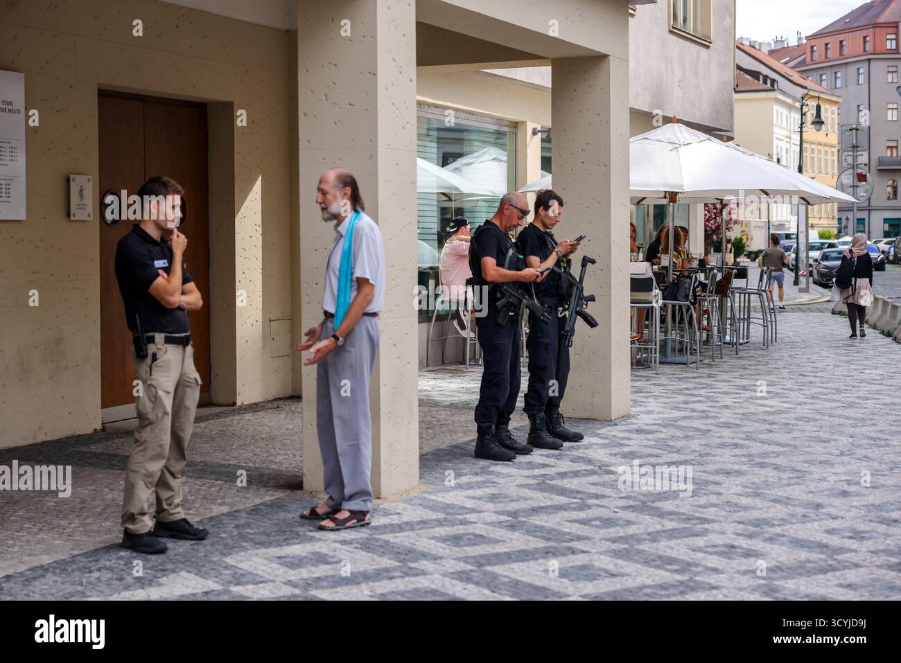 Bewaffnete Polizeibeamte stehen vor einem Café in der Nähe des jüdischen Viertels in Prag, Tschechische Republik, während Fußgänger in der Nähe reden. Stockfoto