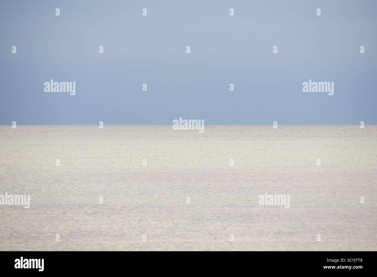 Eine ruhige Küstenszene mit ruhigem, hellem Wasser, das sich in einen sanften blauen Himmel verwandelt. Der Horizont ist kaum sichtbar, was eine minimalistische Komposition mit sich bringt Stockfoto