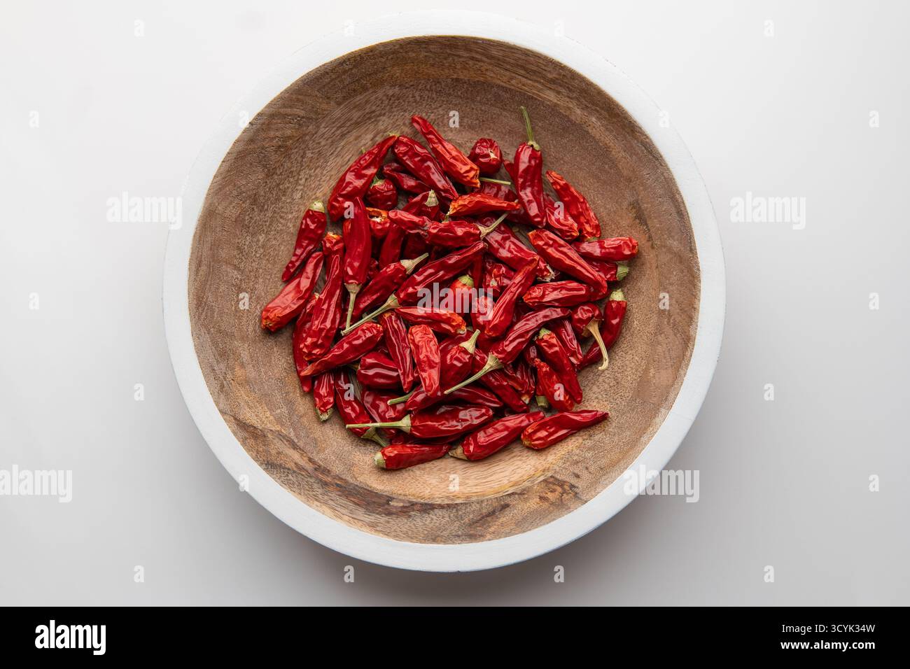 Holzplatte mit weißen Kanten gefüllt mit hellroten getrockneten Chili-Paprika auf weißem Hintergrund Stockfoto