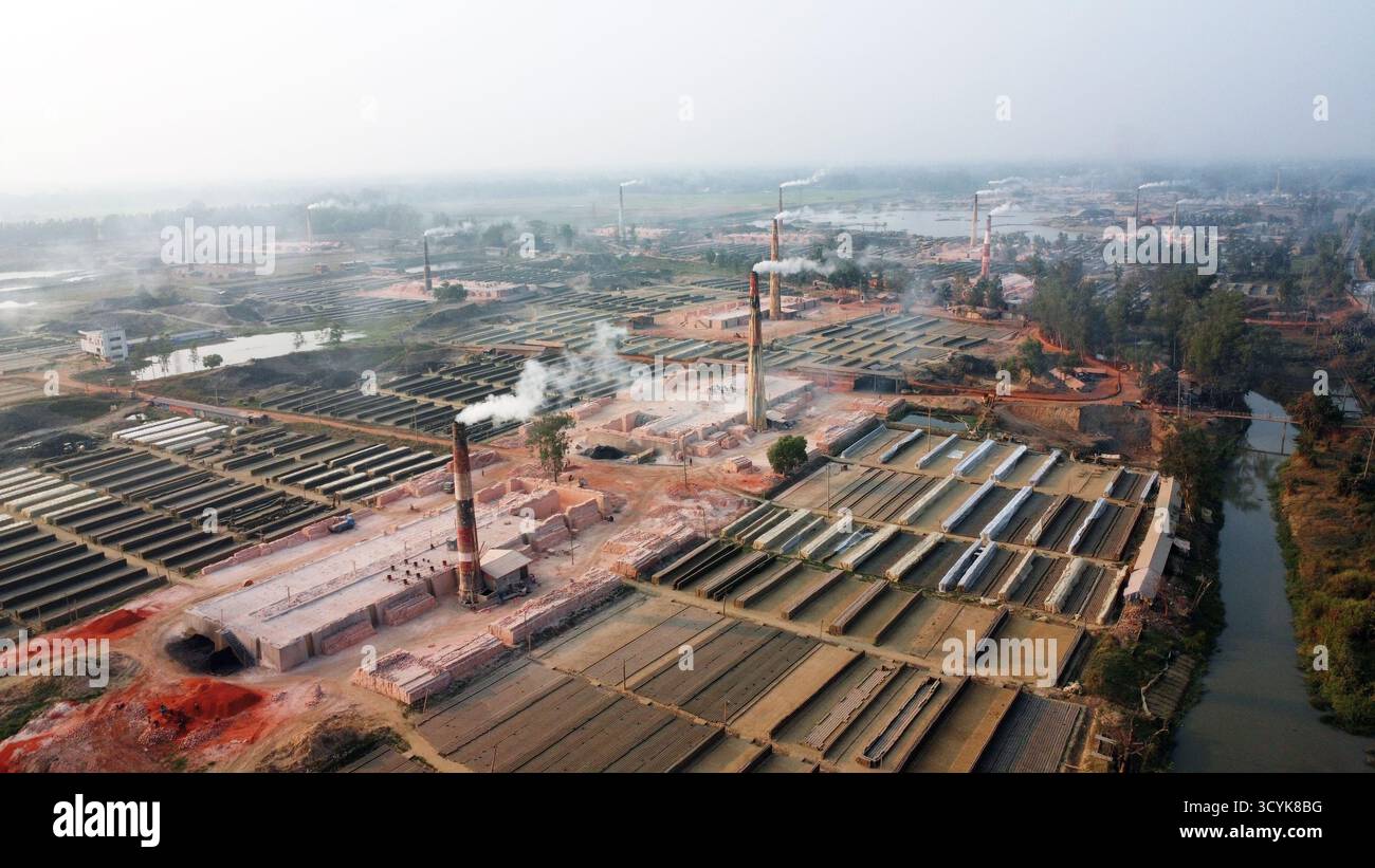 Ein gemauerter Feldkamin setzt Rauch in den Abendhimmel und symbolisiert Industrie und Arbeit in den warmen Abendtönen im ländlichen Bangladesch. Stockfoto