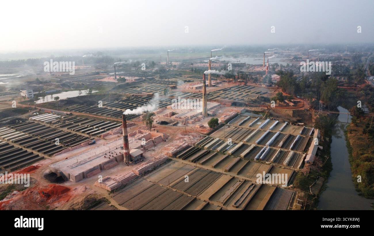 Ein gemauerter Feldkamin setzt Rauch in den Abendhimmel und symbolisiert Industrie und Arbeit in den warmen Abendtönen im ländlichen Bangladesch. Stockfoto