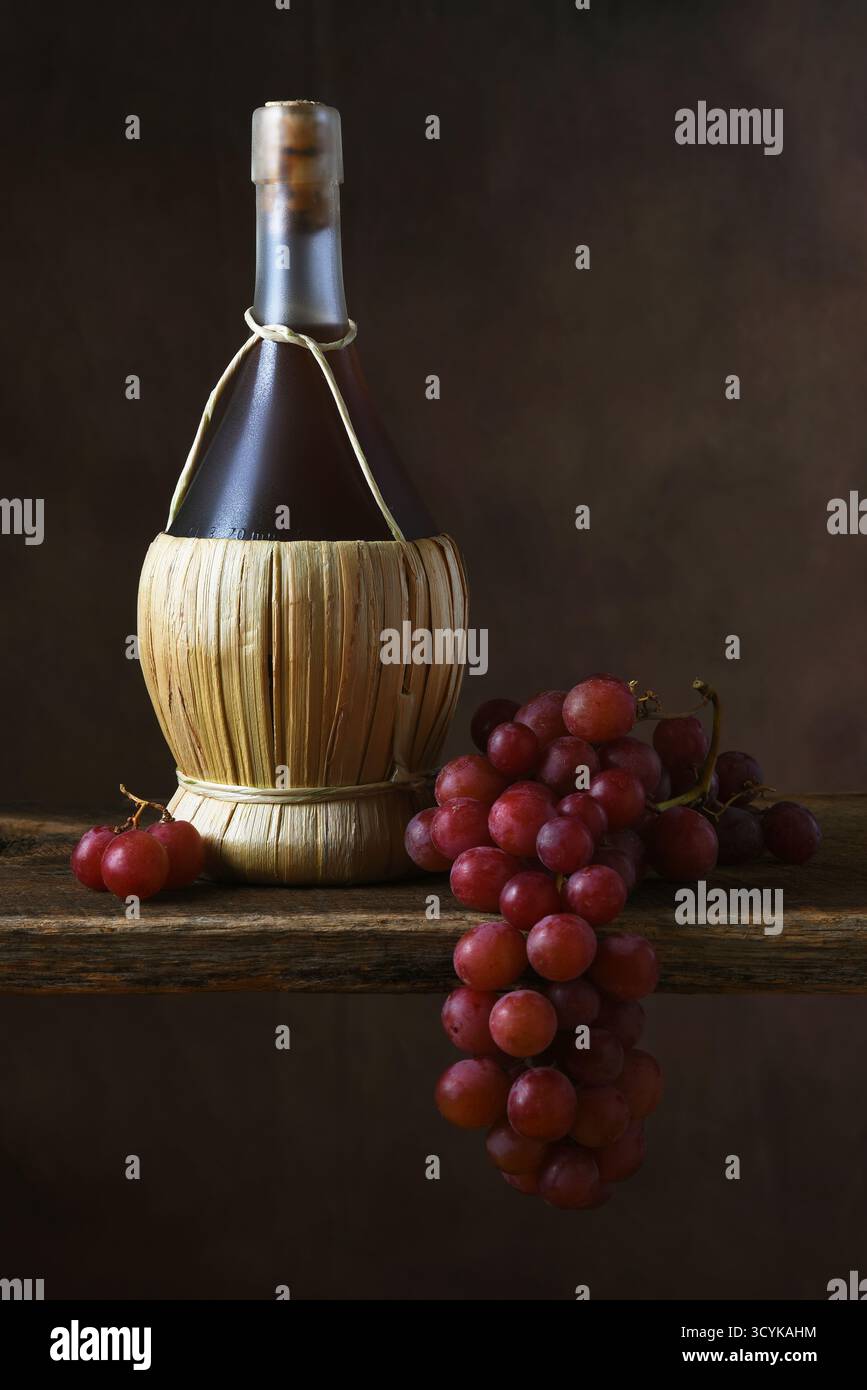 Trauben Chianti Stillleben. Eine Flasche Chianti-Wein und ein Haufen roter Trauben über dem Rand eines rustikalen Holzbretts. Stockfoto