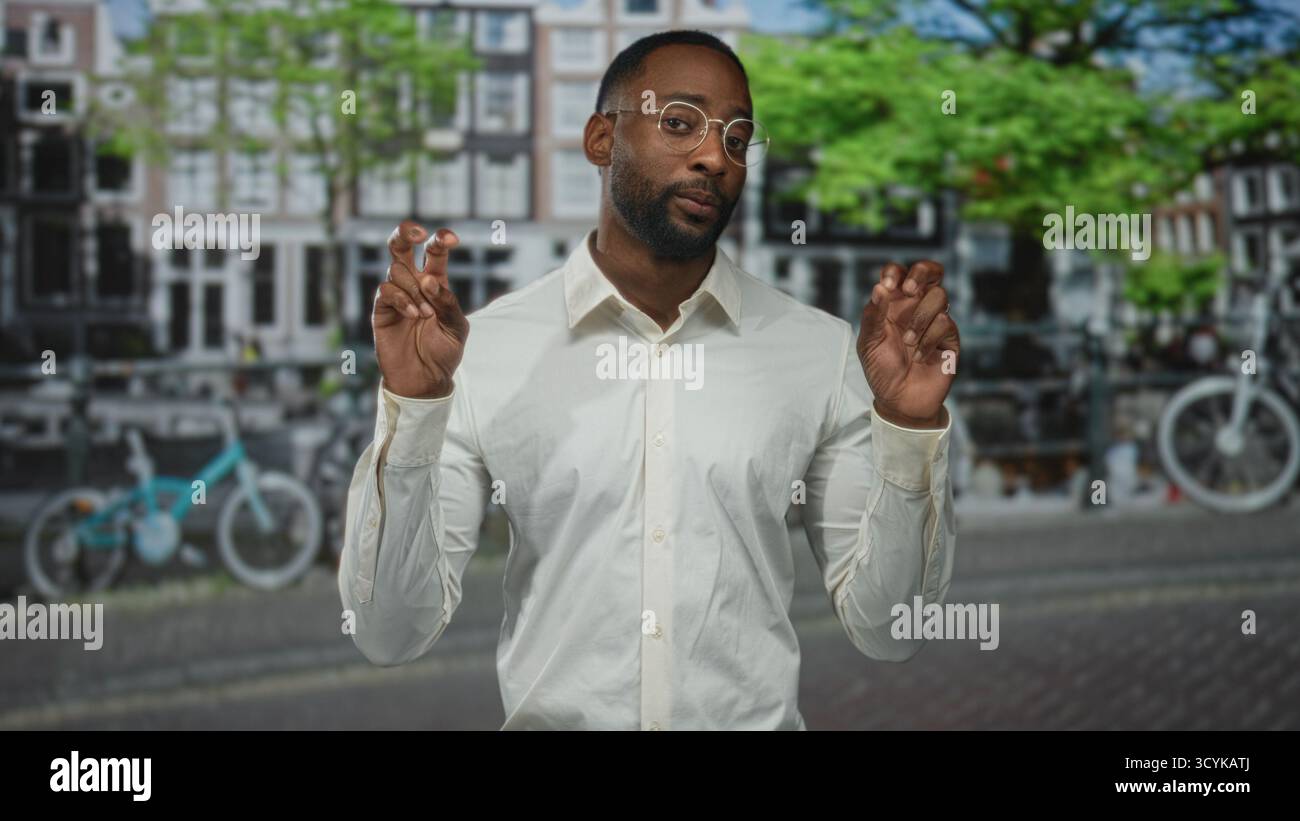 Der Mann macht mit beiden Händen Luftzitierungen auf einer amsterdamer Straße am Kanal, trägt Brille und ein weißes Hemd; sarkastische Kommentare. Stockfoto