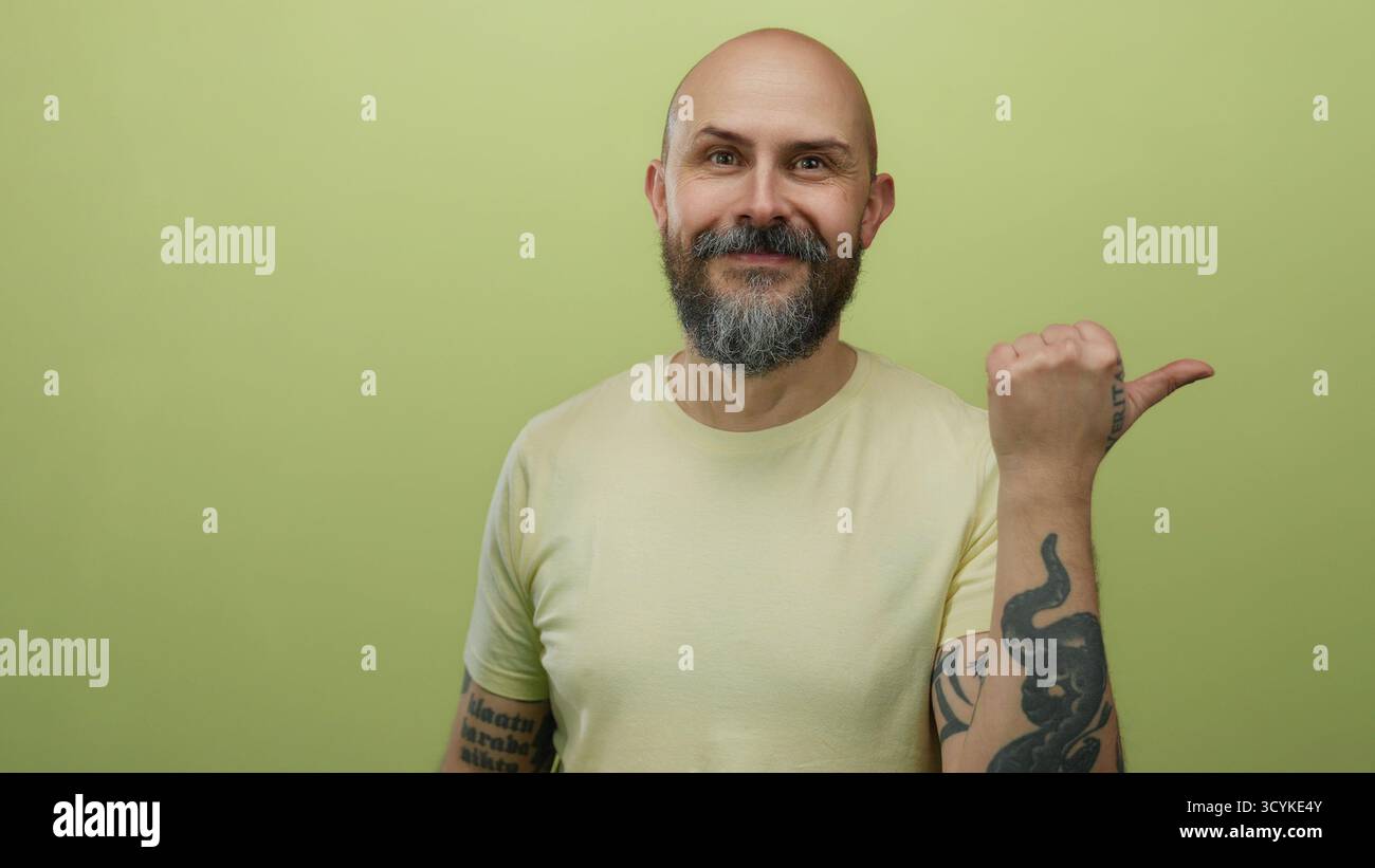 Kahler bärtiger Mann mit Tattoos Gesten mit Daumen vor gelber Wand isolierter Hintergrund Stockfoto