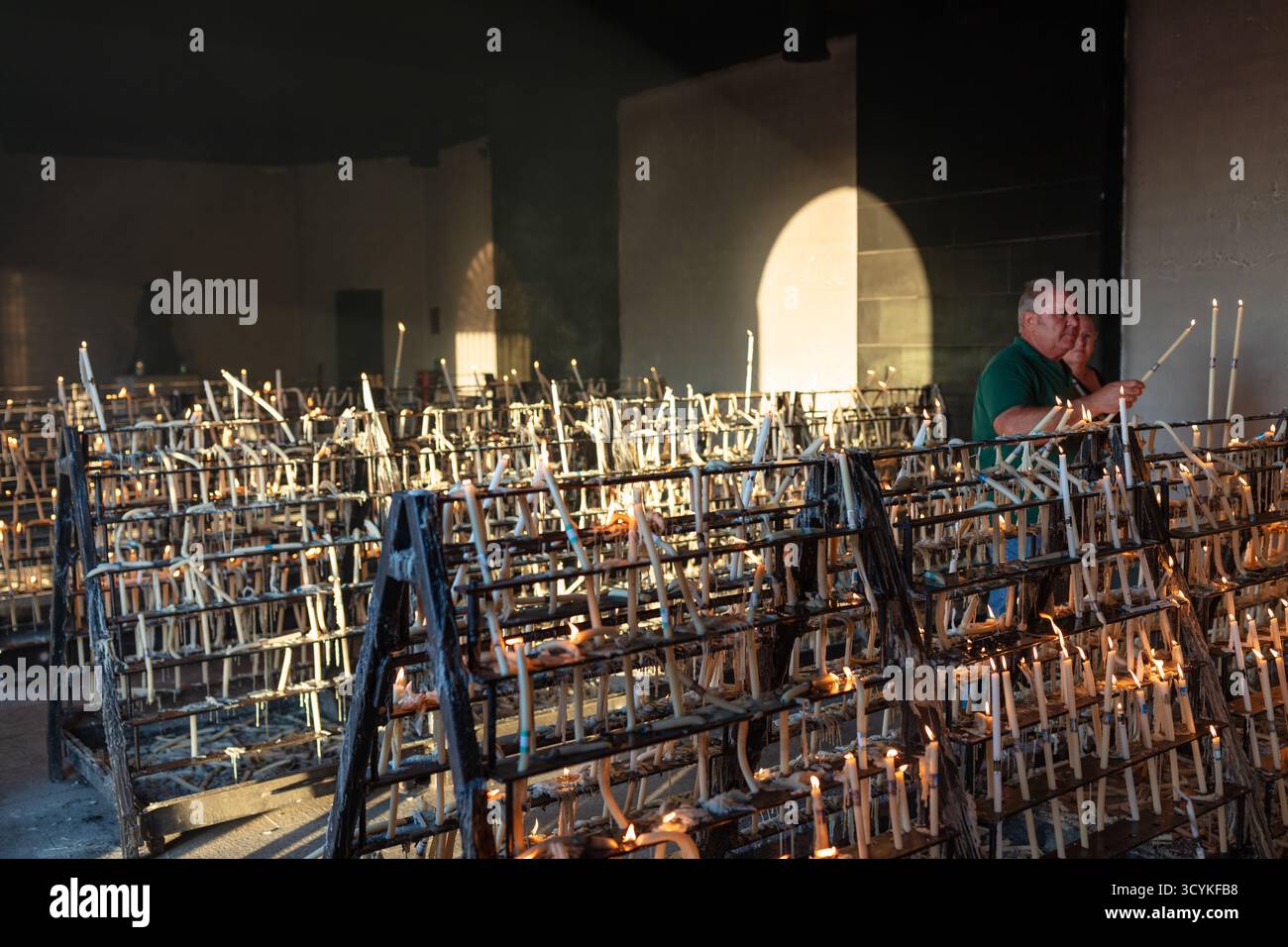 El Rocio, Sevilla, Andalusien, Spanien. August 2025. Eine ältere Frau zündet Kerzen in einer Kapelle als Teil einer religiösen Praxis an. Stockfoto
