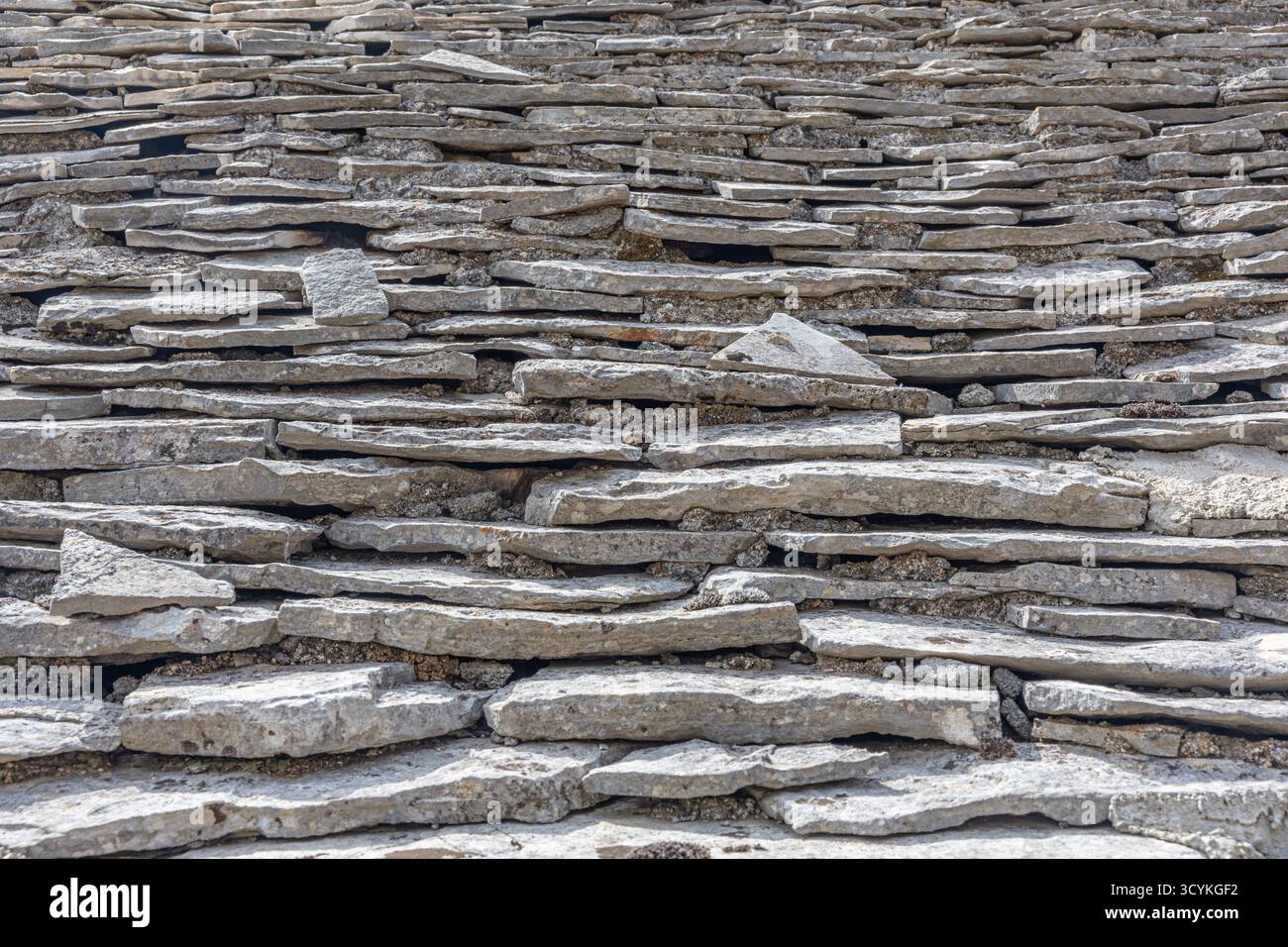 Nahaufnahme eines Trockensteingebirges aus horizontalen, flachen Steinen. Die mehrschichtige Textur und die verwitterten grauen Steine vermitteln rustikalen Charme, Langlebigkeit, und Stockfoto