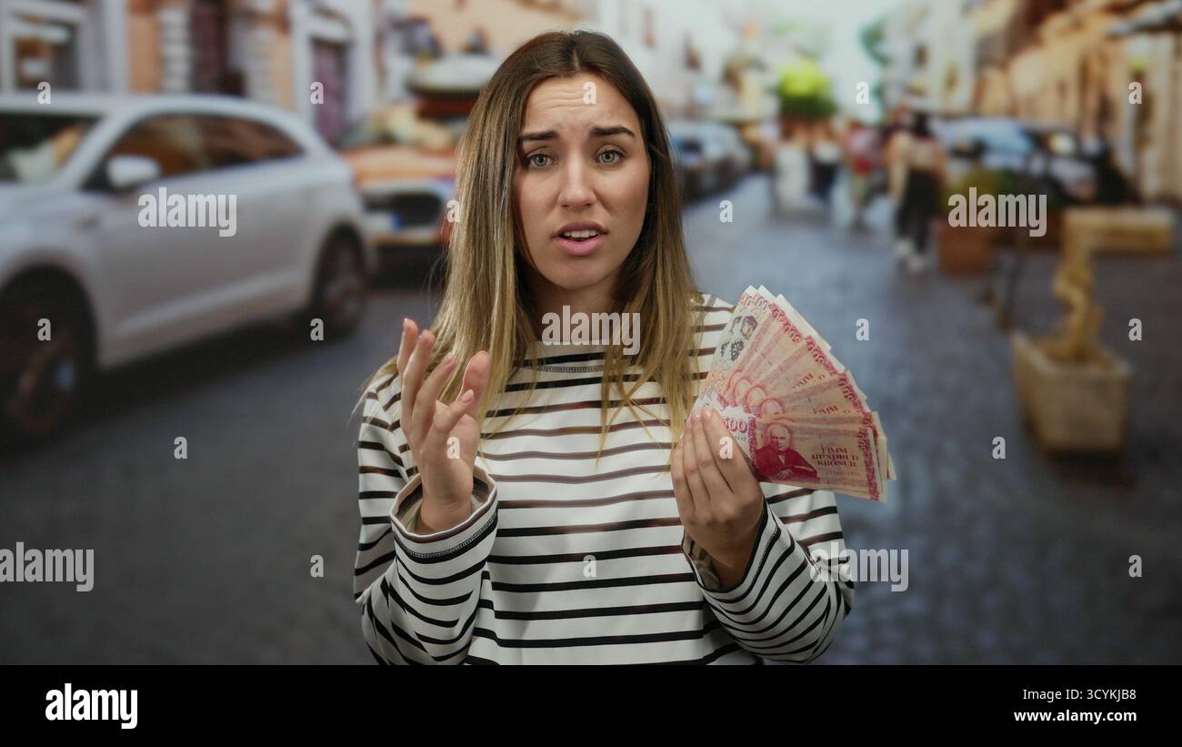 Frau mit isländischem Kronen-Geld auf belebter Straße mit ungezwungenem Ausdruck, die urbane Outdoor-Umgebung mit Fokus auf Finanzen und Alltag erfasst Stockfoto