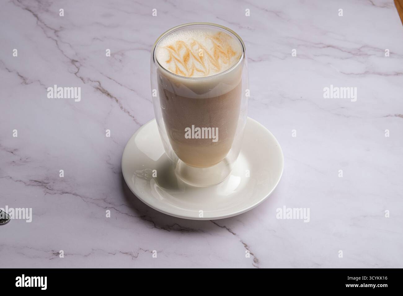 Genießen Sie den köstlichen Caramel Latte, der wunderschön in einem klaren Glas auf einer Marmoroberfläche präsentiert wird Stockfoto