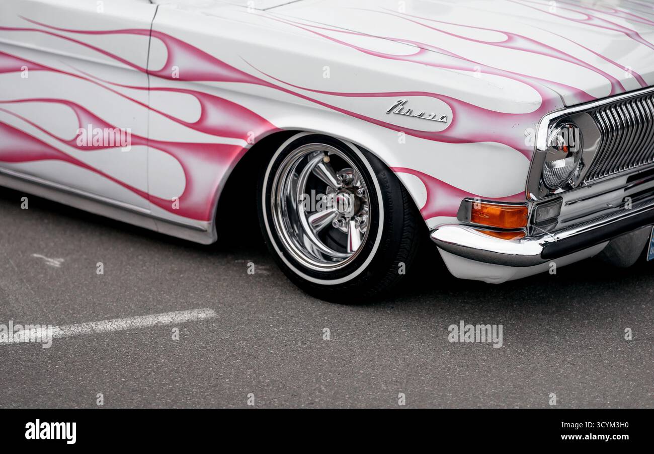 1970er Jahre Volga 24 Limousine mit rosa Flamme an den Seiten und Motorhaube. Nahaufnahme der rechten Ecke eines weißen Oldtimers, der auf einer Straße geparkt ist. Stockfoto