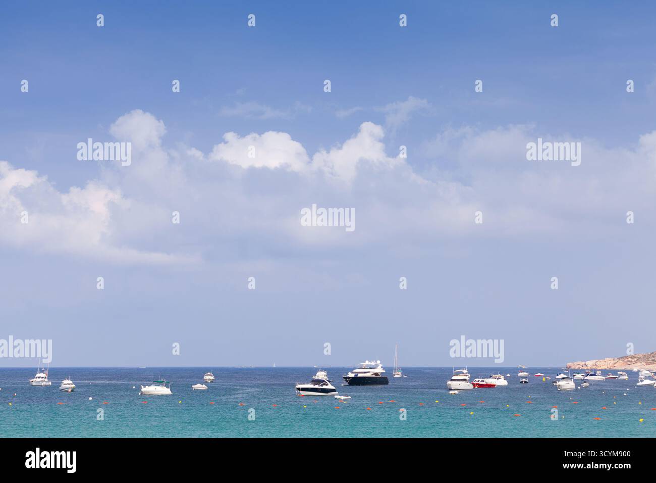 Ein ruhiger Blick auf die Küste mit mehreren kleinen Booten, die in der Nähe einer ruhigen Küste ankern. Hellblauer Himmel, weiche Wolken und türkisfarbenes Wasser bilden einen Peak Stockfoto