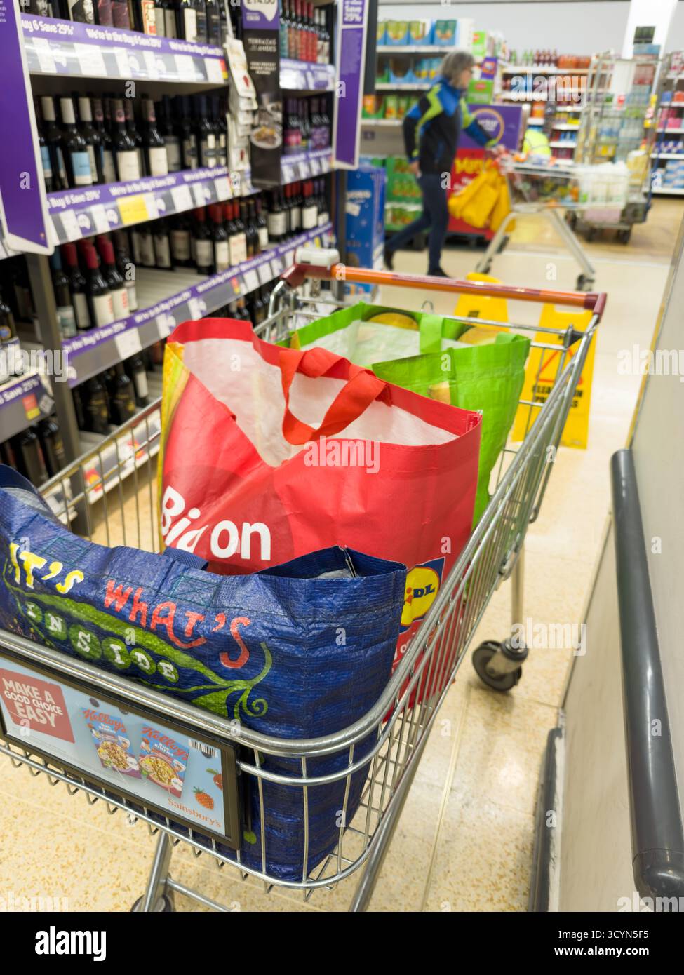 Shopper Using Smart Scanner organisiert farbcodierte wiederverwendbare Einkaufstaschen in einem Trolley und präsentiert moderne Selbstkasse und schnelle Lebensmitteleinkäufe in Großbritannien Stockfoto