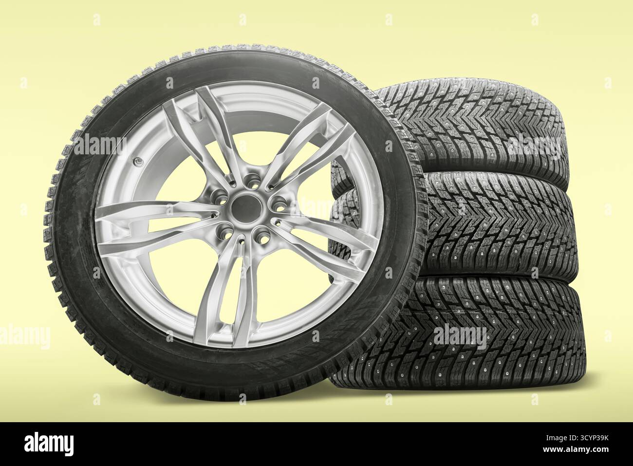 Ein neuer Satz von vier Winterreifen mit Nieten befindet sich neben einer eleganten Leichtmetallfelge, die für den Austausch in einer Reifenwerkstatt vorbereitet wird. Perfekt für winterliche Fahrbedingungen Stockfoto