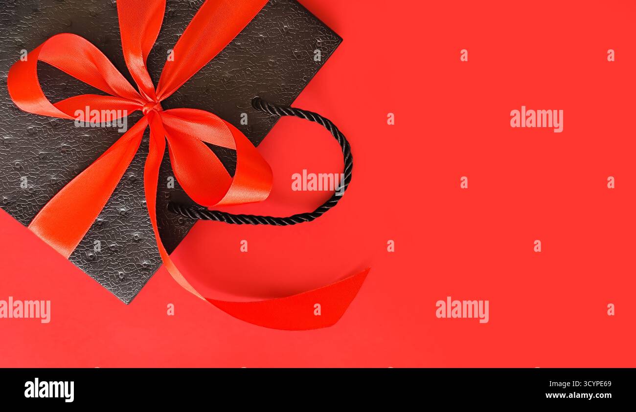 Schwarze Tasche mit roter Schleife auf rotem Hintergrund mit Platz für Text. Hochwertige Fotos Stockfoto