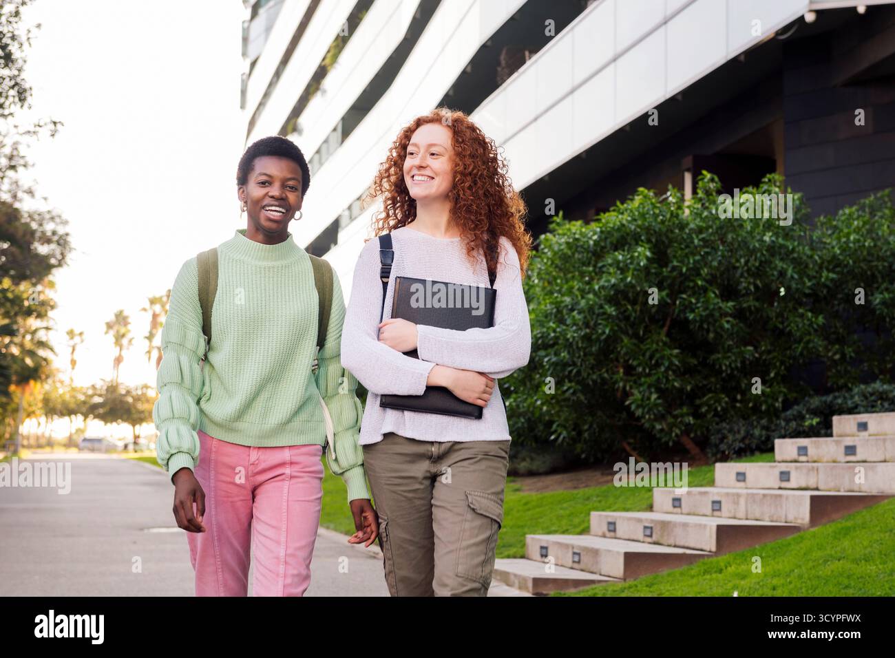 Zwei junge Studenten lächeln und gehen die Straße runter Stockfoto