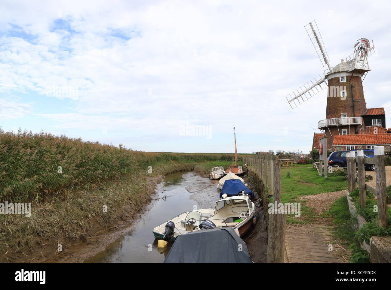 Blick auf Cley Mill und Kai mit Booten auf dem Fluss Glaven bei Niedrigwasser an der Küste von North Norfolk bei Cley Next the Sea, Norfolk, England, Großbritannien. Stockfoto