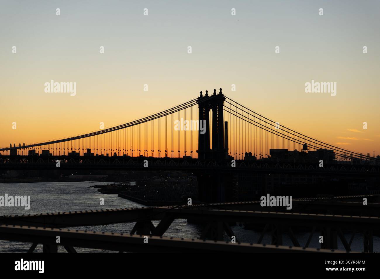 Die legendäre Manhattan Bridge steht vor einem warmen, abfallenden Sonnenaufgangshimmel über dem East River in New York City. Stockfoto